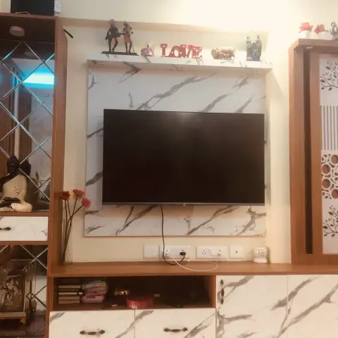 Living room TV unit in white marble-finish laminate flanked by a mirrored diamond-pattern display cabinet holding a Buddha statue