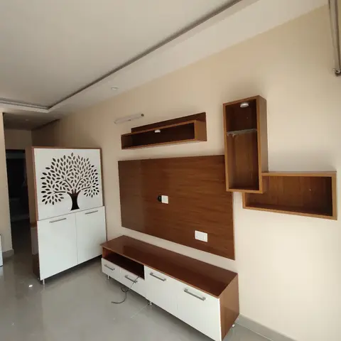 Living room TV unit wall in walnut laminate with asymmetric floating display boxes and a white cabinet with a carved tree-motif door.