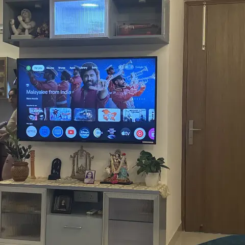 Living room TV unit wall with a fluted glass-front storage cabinet, an upper display shelf with a backlit frosted-glass niche, and a console styled with idols