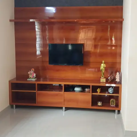 Living room TV unit wall with a glossy cherry-wood laminate panel below a dark grey textured paint band, and an open console styled with brass figurines.