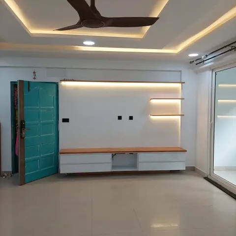 Living room TV unit wall with a floating wood-and-white console, backlit open shelving, and a cove-lit stepped false ceiling with a wood-blade fan