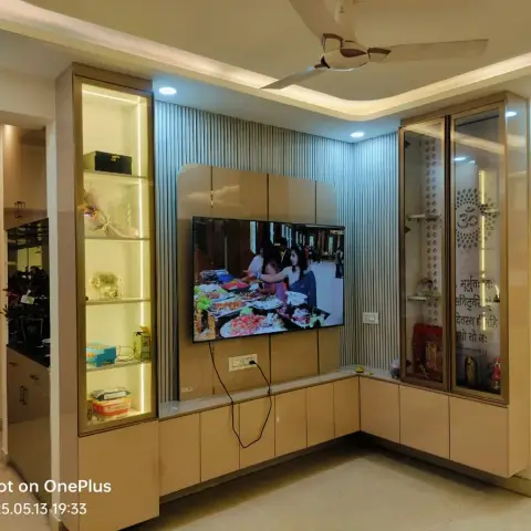 Living room TV unit with a fluted panel backdrop, open display shelving, and a glass-fronted pooja cabinet etched with Om.