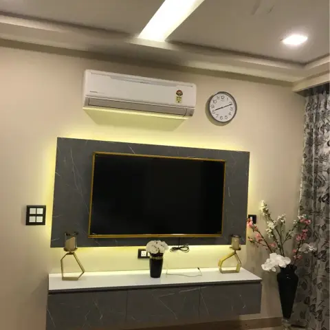Living room TV unit with a backlit grey marble-effect panel in a gold frame, floating white console styled with gold candle stands and vases below