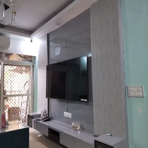 Living room TV unit with fluted grey panelling behind a wall-mounted television, above a glossy low console with drawers and glass display niches.
