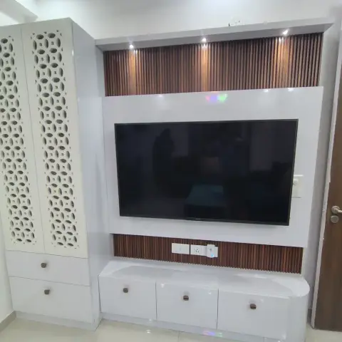 Living room TV unit with white CNC jaali-pattern cabinet doors and vertical fluted wood panelling as the backdrop for the wall-mounted television.