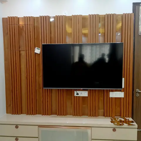 Living room TV wall clad in vertical fluted wood panelling with a wall-mounted television over a cream TV unit with rose-gold drawer pulls.