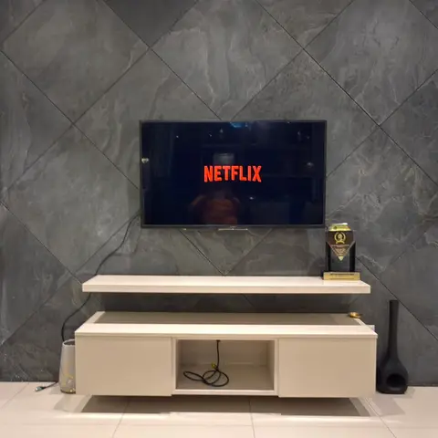 Living room TV wall clad in diagonally laid grey marble-effect tiles, with a floating white lacquered TV console below.