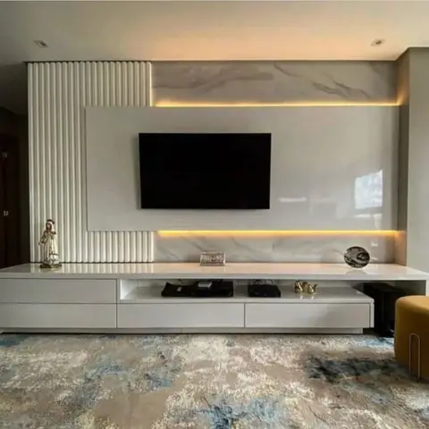 Living room TV wall combining a white fluted panel with a backlit marble slab, a long floating white console styled with a statue and decorative plate