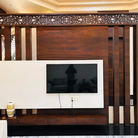 Living room TV wall framed by an ornately carved wood jaali border around a rosewood-veneer panel, with a floating drawer console below.