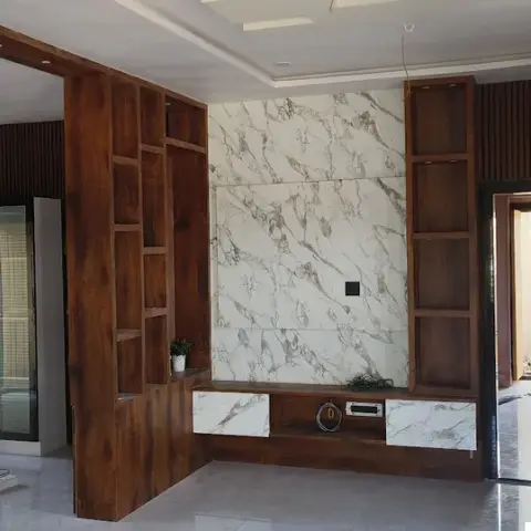 Living room TV wall in book-matched white marble flanked by open wood display shelving, seen from an adjoining fluted-panel hallway