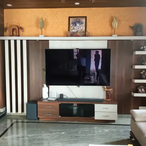 Living-room TV wall in dark walnut veneer with white fluted battens to the left, an ochre textured band above holding a framed Krishna painting and brass leaf