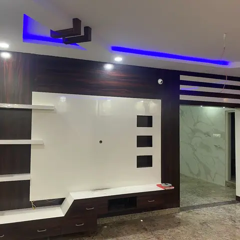 Living-room TV wall in dark wood panelling with a glossy white display unit and blue LED cove lighting in a stepped false ceiling.
