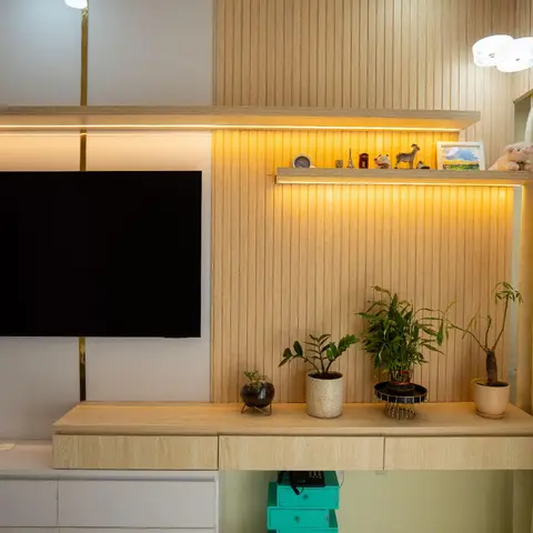 Living room TV wall in fluted light-wood panelling with brass inlay strips, a floating console styled with potted plants beneath a dandelion pendant light.