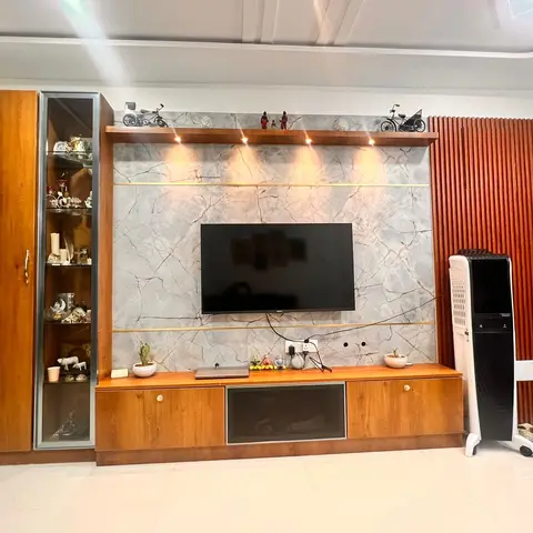 Living room TV wall in honey-toned wood joinery with a grey-veined marble backsplash and spotlighting