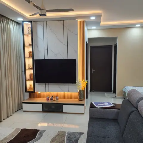 Living room TV wall in marble-look panels flanked by a slim backlit niche holding brass idols and a fluted wood strip