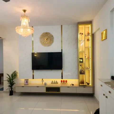 Living room TV wall in patterned off-white wallpaper edged with gold strips, a gold sunburst clock above the screen and a backlit gold display column