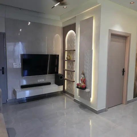 Living room TV wall in polished marble cladding beside a backlit fluted-stone niche displaying a Buddha statue, with a floating white TV console below.