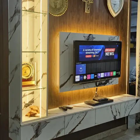 Living-room TV wall in walnut veneer with white marble-look panels, a tall backlit glass-shelf niche holding a gold award trophy