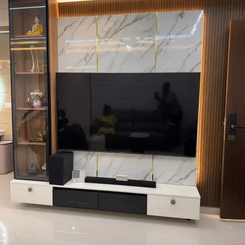 Living room TV wall in white marble-look slabs split by thin brass inlay strips, framed by fluted teak panelling and a slim black-framed glass display column