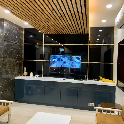 Living-room TV wall of black glass panels gridded in brass beside a dark gold-veined marble pier