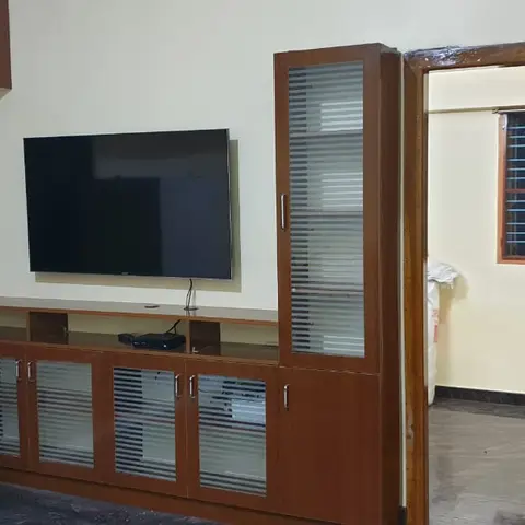 Living room TV wall unit in glass-and-wood cabinetry, seen alongside a carved wooden main door with a Buddha-motif knocker.