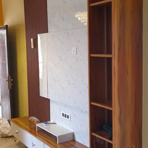 Living room TV wall unit with a floating wood-and-marble-effect console, a tall wooden display shelf tower, and dining chairs in the foreground.