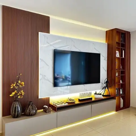 Living-room TV wall where a white-veined marble-look panel carrying the TV sits between a full-height fluted teak wall on the left and a slim teak open-shelf