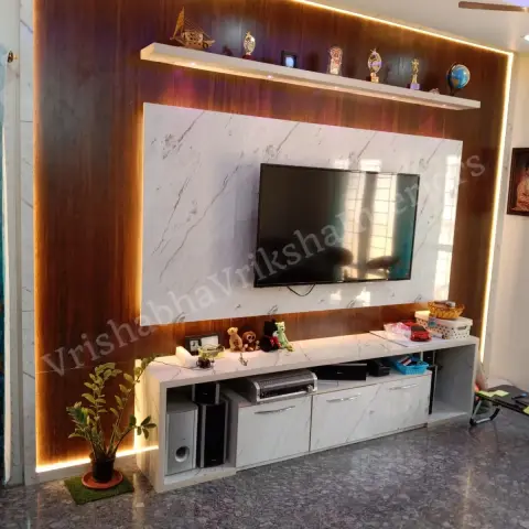 Living-room TV wall with a walnut-toned veneer panel edge-lit in warm LED, a white marble-look floating console and a trophy display shelf above the screen