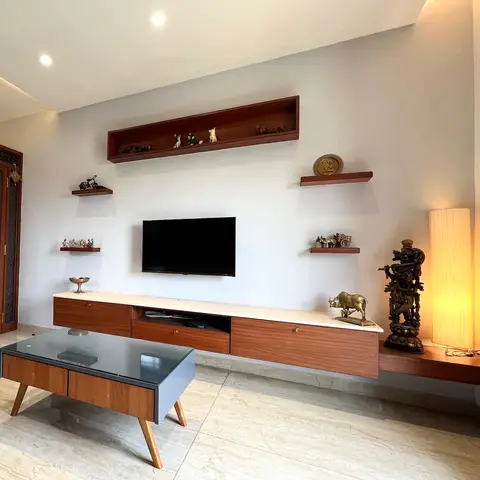 Living room TV wall with a floating walnut console under a marble-look top, open shelves styled with brass figurines and a tall brass deity statue beside a