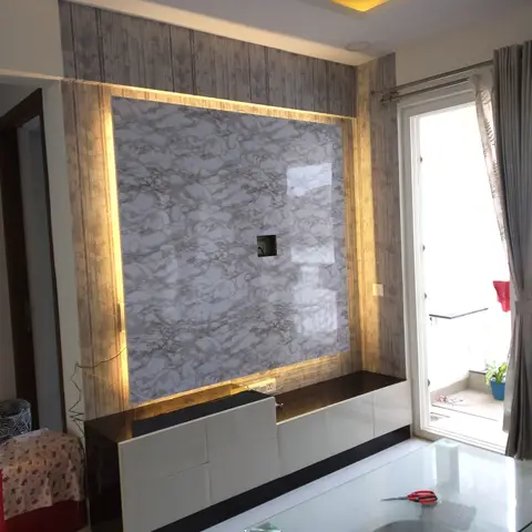Living room TV wall with a backlit grey-marble-effect panel framed in gold woodgrain wallpaper trim, glossy black-and-white floating console below