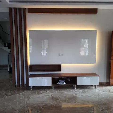 Living room TV wall with a backlit glossy grey panel flanked by fluted wood pillars, a floating walnut-and-white TV console with an open display niche