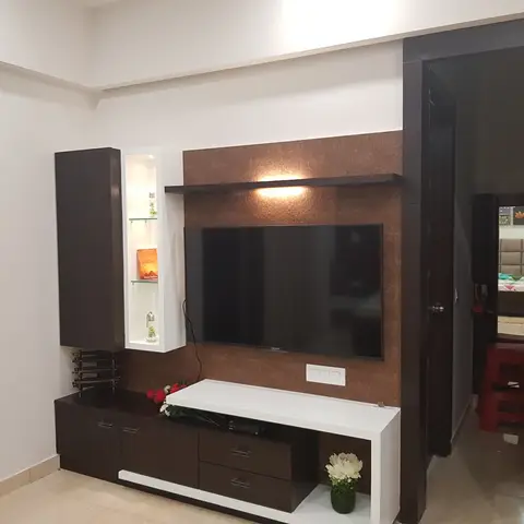 Living room TV wall with a dark-wood and white lacquer entertainment unit set against a textured bronze panel, open to a bedroom beyond.