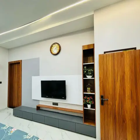 Living room TV wall with a floating grey media console, wood-tone panel behind the screen, and an open display shelf with plants beside a wood-veneer door.