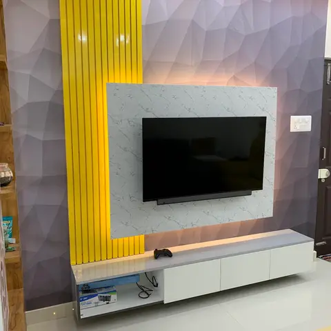 Living room TV wall with a marble-look panel, backlit yellow fluted trim, and a faceted geometric textured wall finish beside the entrance door.