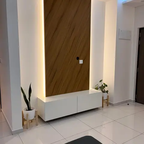 Living room TV wall with a backlit wood veneer panel, white floating console, and potted plants on wooden stands flanking either side.