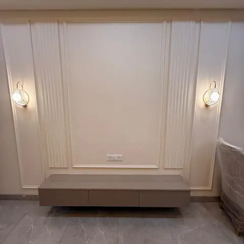 Living room TV wall with a fluted moulded panel and gold wall sconces flanking a floating taupe console, ready for furniture install.