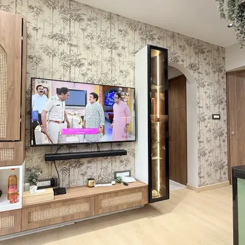 Living room TV wall with a cane-front storage unit, bamboo-leaf wallpaper backdrop, and a backlit glass display nook beside an archway toward the kitchen.