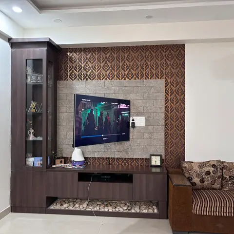 Living room TV wall with a copper leaf-pattern wallpaper panel, stone-clad tile backdrop, and a dark wood console lined with white pebbles.