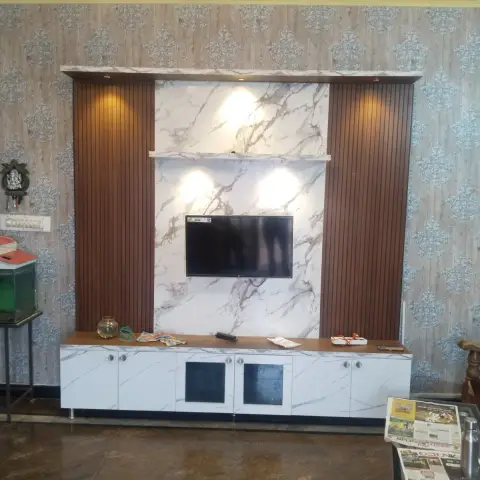 Living-room TV wall with a book-matched white marble slab backdrop flanked by vertical wood-fluted panels, a floating display shelf with spotlights