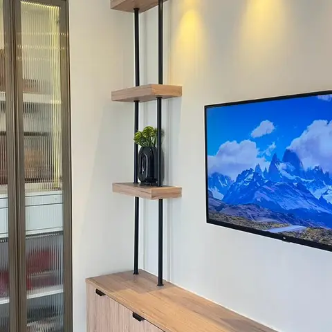 Living room TV wall with a floating wood console, vertical black-rod shelving unit with accent spotlights, and a fluted-glass display cabinet alongside.