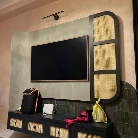 Living room TV wall with a cane-webbed black floating unit, olive textured tile accent, and a lime-plaster feature wall behind the screen.