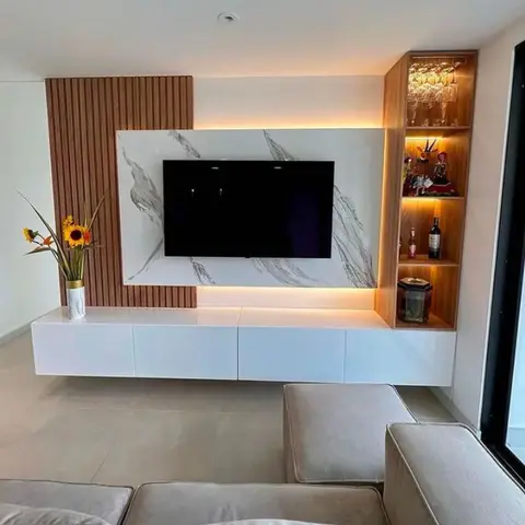 Living room TV wall with a white marble-effect backdrop, fluted wood side panelling, a backlit bar display niche with glassware and a floating white console.