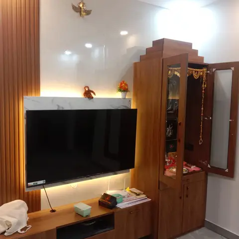 Living room TV wall with a marble-look backlit panel and an adjoining wood pooja unit with mirrored doors and temple idols.