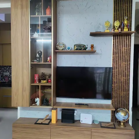Living room TV wall with a wood-and-marble media unit, a tall glass-door display cabinet filled with travel souvenirs and trophies