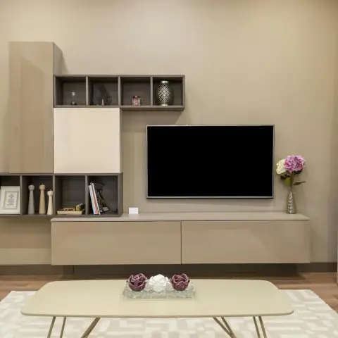 Living room TV wall with a taupe modular cabinet featuring open cubby shelving styled with decor accessories, patterned drapes