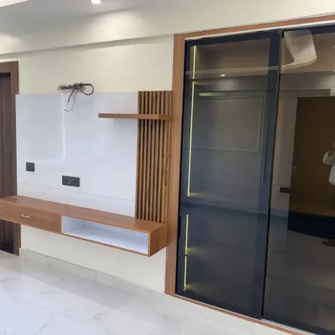 Living room TV wall with a floating wood console and fluted panel backdrop beside a tall black-framed glass wardrobe with internal LED lighting