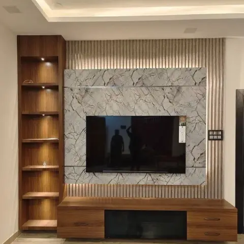 Living room TV wall with a book-matched marble slab backdrop framed by fluted brass-toned panelling, beside a lit wood open-shelf display unit.