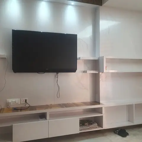 Living room TV wall with book-matched marble-effect stone panelling and a floating white lacquered TV console with asymmetric open shelving, spotlights
