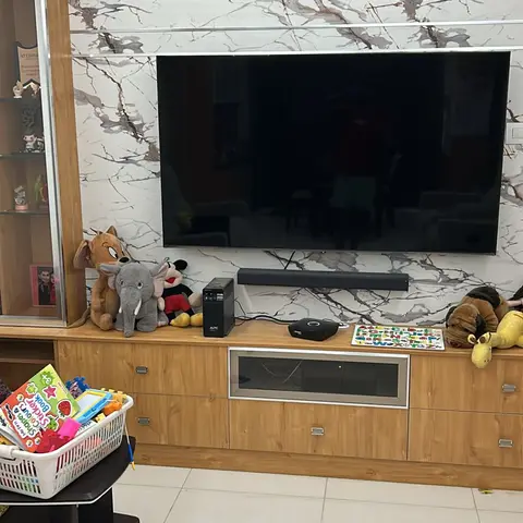 Living room TV wall with book-matched marble slab cladding above a wood-finish console, a display cabinet to one side, and children's toys on the floor.
