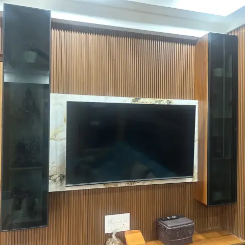 Living room TV wall with fluted wood panelling, a marble-clad TV backdrop, and tall smoked-glass display cabinets flanking the screen.